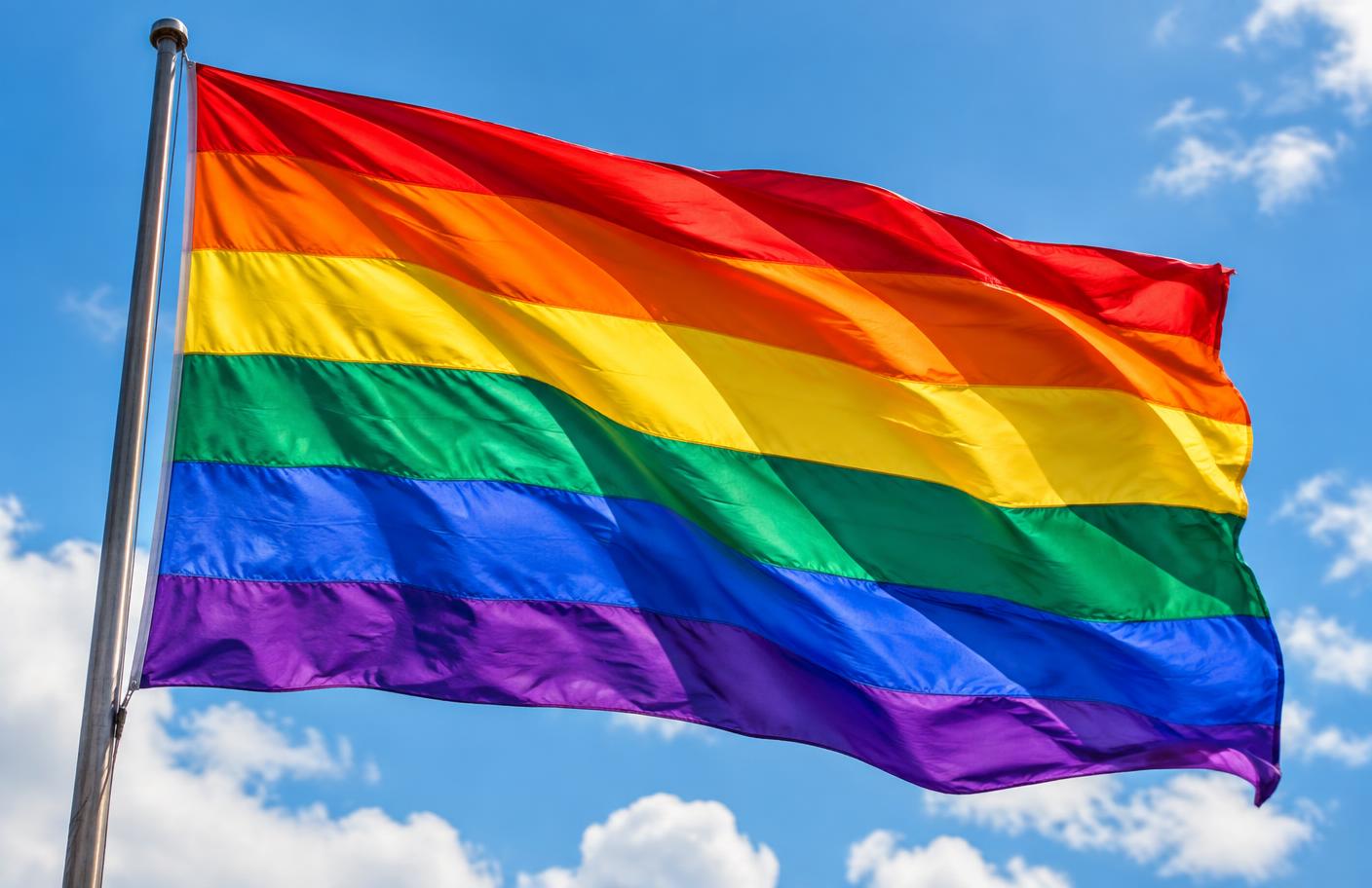 Bandeira arco-íris do orgulho LGBTQIA+ tremulando sob céu azul